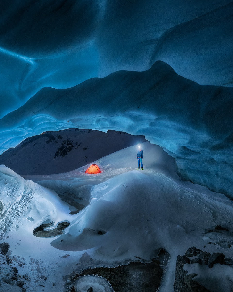 Person with the Betty BT in an ice cave, an illuminated tent in the background