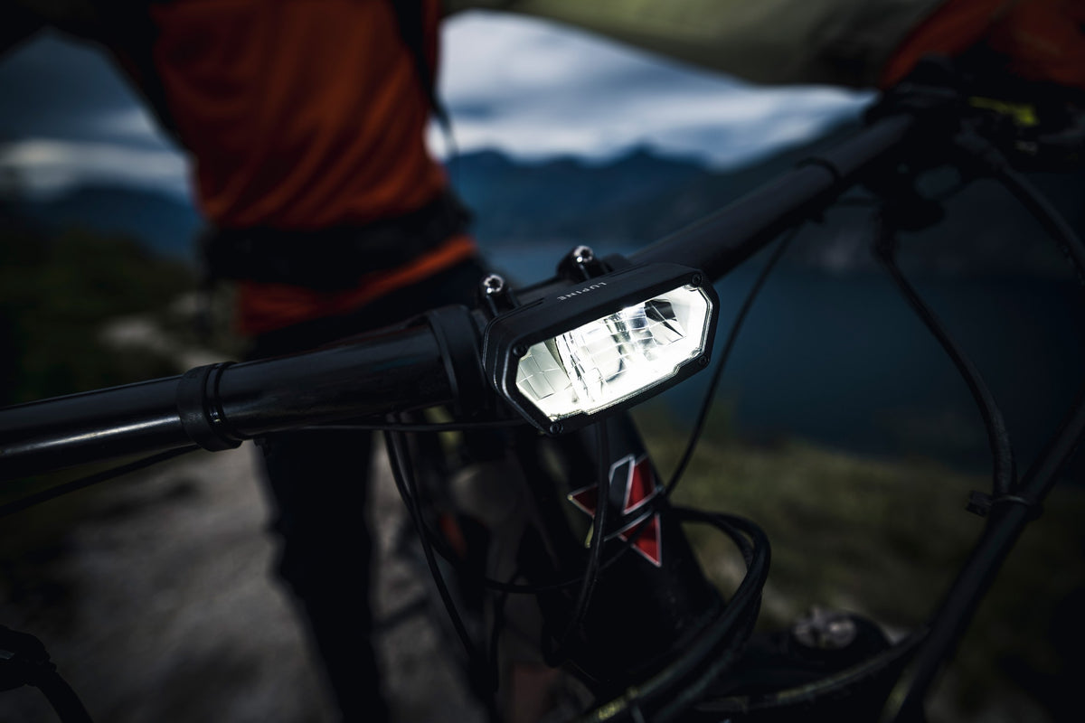 Lupine SL Minimax AF eingeschaltet am Lenker eines Mountainbikes, im Hintergrund Berge und ein See