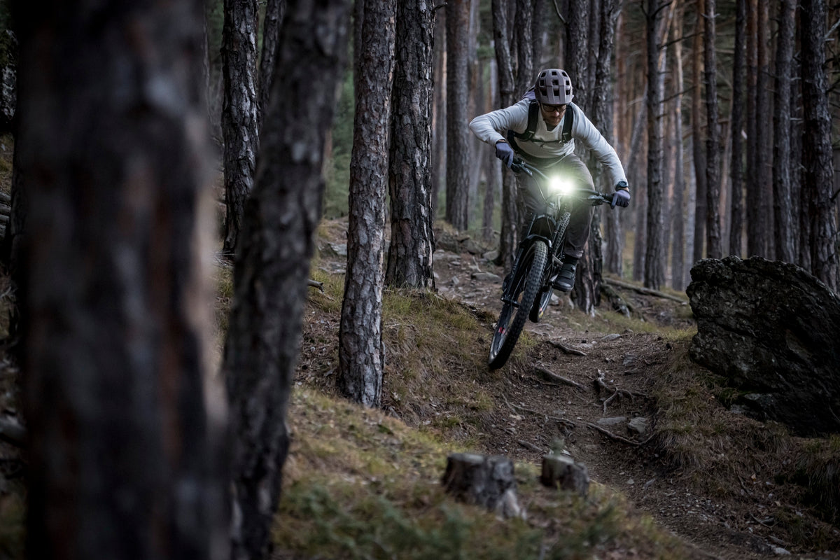 E-Mountainbiker mit eingeschalteter SL X auf einem Waldtrail in der Dämmerung