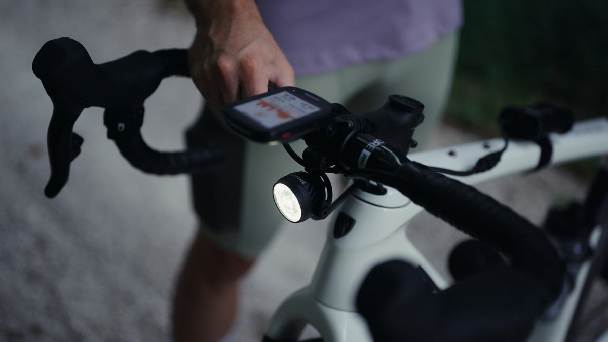 Lupine SL Nano AF switched on at the handlebar of a gravel bike at dusk, hand on the bike computer