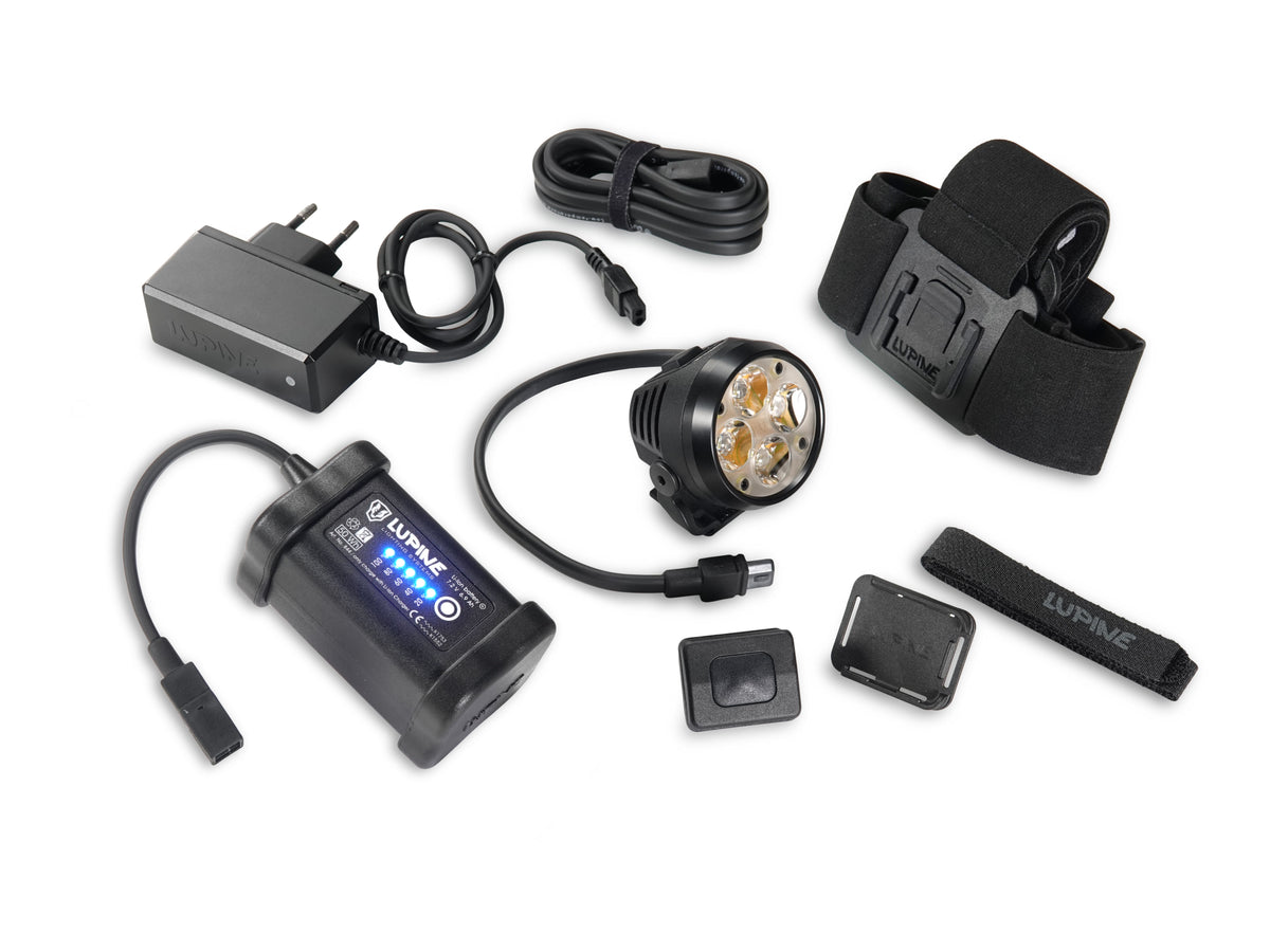 Teile des Lieferumfangs: Wilma Lampenkopf, 6.9 Ah SmartCore-Akku, Bluetooth-Fernbedienung mit Armbandhalter, FrontClick-Stirnband, Verlängerungskabel und Ladegerät Wiesel